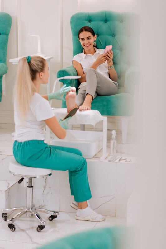Professional blonde-haired chiropodist using feet scrubber